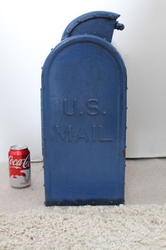 a blue mailbox sitting on top of a white rug next to a soda can