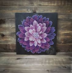 a purple and pink flower is on a black canvas with wood planks in the background