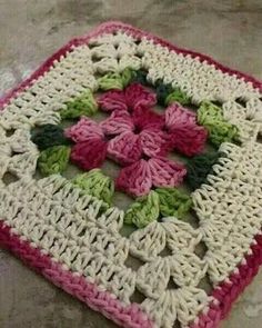 a crocheted square with pink, green and white flowers on it sitting on the floor