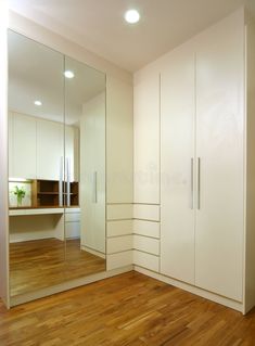 an empty room with wooden flooring and white cabinets in the corner, along with a large mirror on the wall