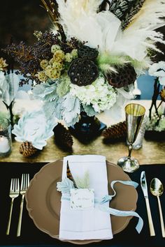 a place setting with feathers, flowers and napkins on the table for an elegant dinner