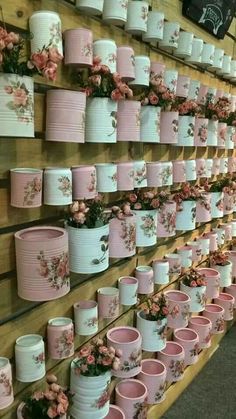 many pink and white cups are hanging on the wall with flowers in them, all lined up