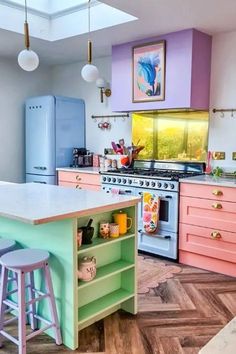 a kitchen with pink, blue and green cabinets and an island in front of the stove