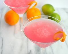 two glasses filled with pink lemonade next to oranges and limes on a table