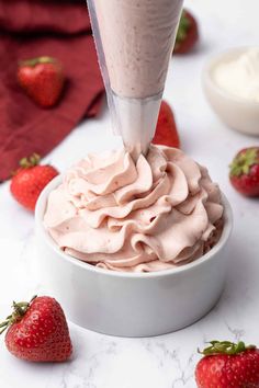 someone is pouring whipped cream into a bowl with strawberries