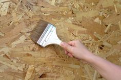 a person holding a brush on top of plywood flooring that has been chipped