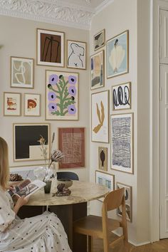 a woman sitting at a table in front of a wall covered with pictures and flowers