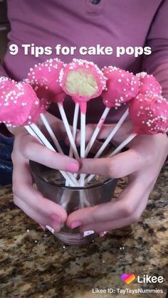 a person holding a cup filled with pink cake pops