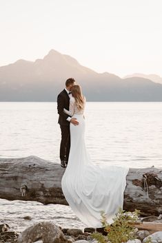 a bride and groom standing on a log by the water