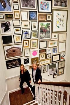 two women are standing on the stairs in front of a wall full of framed pictures