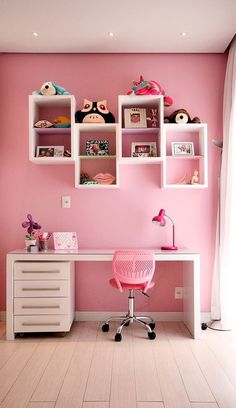 a room with pink walls and white shelves on the wall, along with a desk