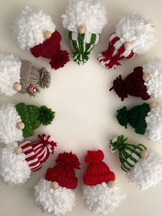 a group of knitted santa hats arranged in a circle on a white surface with green and red pom - poms