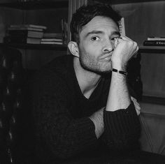 a black and white photo of a man sitting at a desk with his hand on his face