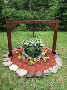 a wooden frame with flowers in the middle on top of a rock and grass area