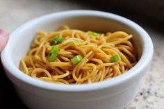 a white bowl filled with noodles and green onions on top of a table next to a fork