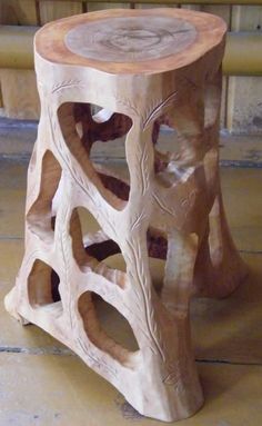 a wooden stool made out of wood with carved designs on the top and bottom, sitting in front of a bench