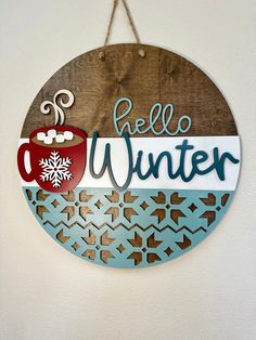 a wooden sign that says hello winter with a cup of coffee hanging from the side