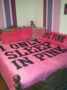 a bed with pink and black comforter on top of it in a room that has striped walls