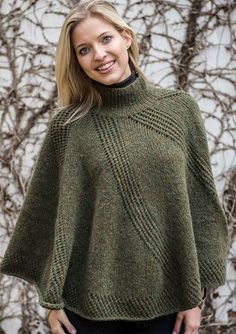 a woman standing in front of a wall wearing a green knitted ponchy