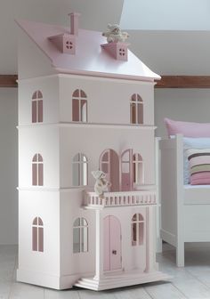 a doll house with pink walls and white trim on the top floor, sitting in front of a bed