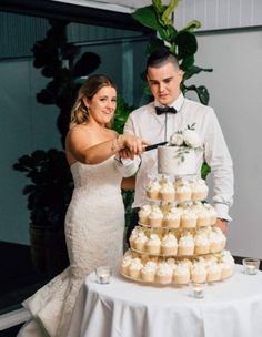 a bride and groom cutting their wedding cake at the reception table with cupcakes in front of them