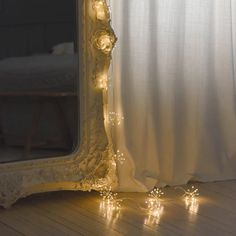 a mirror sitting on top of a wooden floor next to a window covered in lights