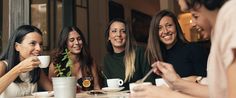 four women sitting at a table drinking coffee and laughing with each other in front of them