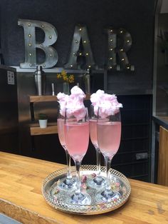 two champagne flutes with pink flowers in them sitting on a silver platter at a bar