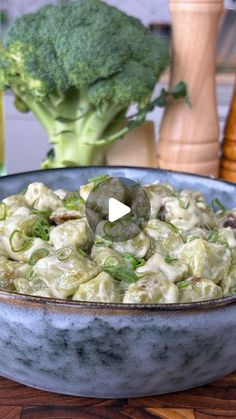 a bowl filled with pasta and broccoli on top of a wooden table next to a vase