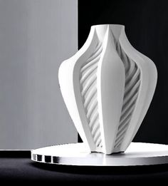 a white vase sitting on top of a table next to a black and white wall