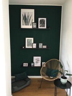 a living room with green walls and pictures hanging on the wall above a wicker chair