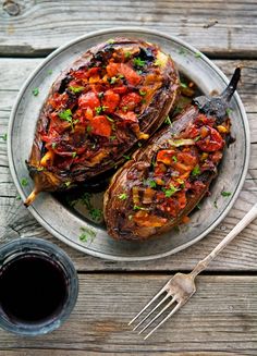 two stuffed eggplant halves on a plate next to a fork and cup of coffee