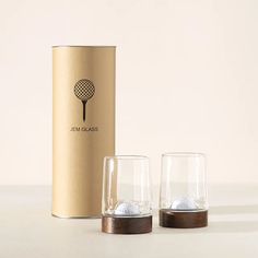 two glasses sitting next to each other in front of a canister with golf balls inside