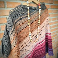 a multicolored crocheted sweater hanging on a brick wall next to a wooden hanger