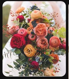 a woman holding a bouquet of flowers in her hands and wearing a white dress with red, orange, yellow and pink flowers on it