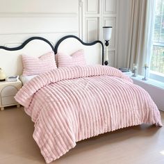 a bed with pink comforter and pillows in a bedroom