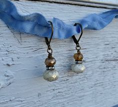 two white and brown beads are hanging from earwires on a blue ribbon attached to a piece of wood