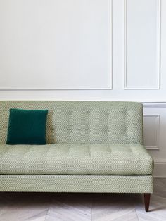 a green couch sitting on top of a hard wood floor next to a white wall