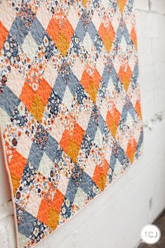 an orange and blue quilt hanging on a white brick wall