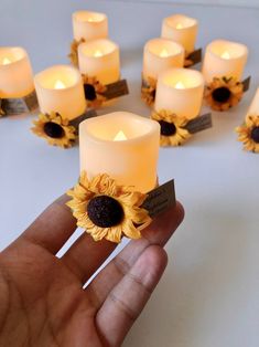 a hand holding a bunch of candles with sunflowers on them in front of it