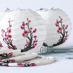 three white paper lanterns decorated with pink flowers and birds on them, sitting next to wire