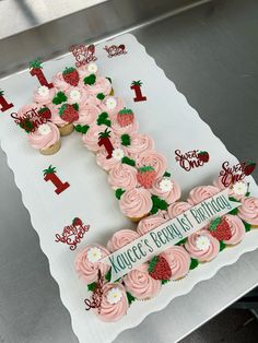 a cake that is shaped like the letter f with cupcakes and strawberries on it