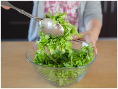 a person scooping lettuce out of a glass bowl with a metal spoon