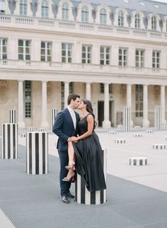 a man and woman kissing in front of a large building with columns on the ground