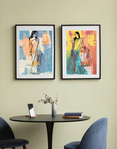 two paintings hang on the wall above a small table with chairs and a phone in front of it