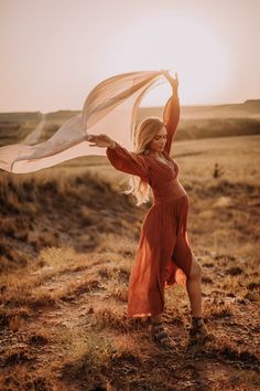 a woman in an orange dress is holding a white scarf over her head while standing on a field