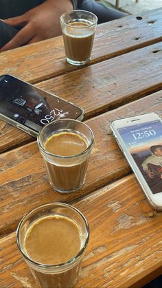 two cups of coffee sit on a wooden table next to an iphone and another cell phone