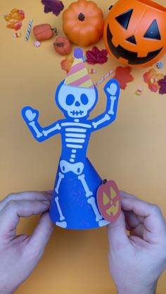 someone is holding up a paper skeleton with a party hat and pumpkins in the background