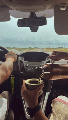 two people are sitting in the driver's seat of a car and one is holding a cup