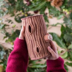 a woman holding up a knitted cup cozying it's sleeve with holes